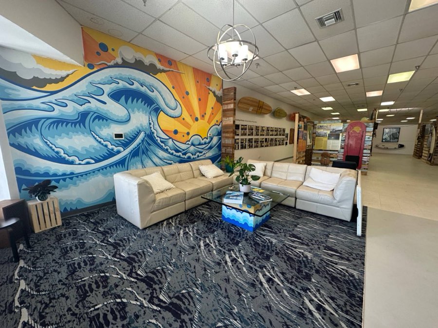 The museum lounge, with a sectional sofa in front of a wave-and-sunrise mural, and the galleries beyond