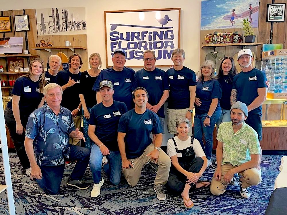 Members of the Surfing Florida Museum crew in navy museum tees, gathered in front of the sanderling sign in the gift shop